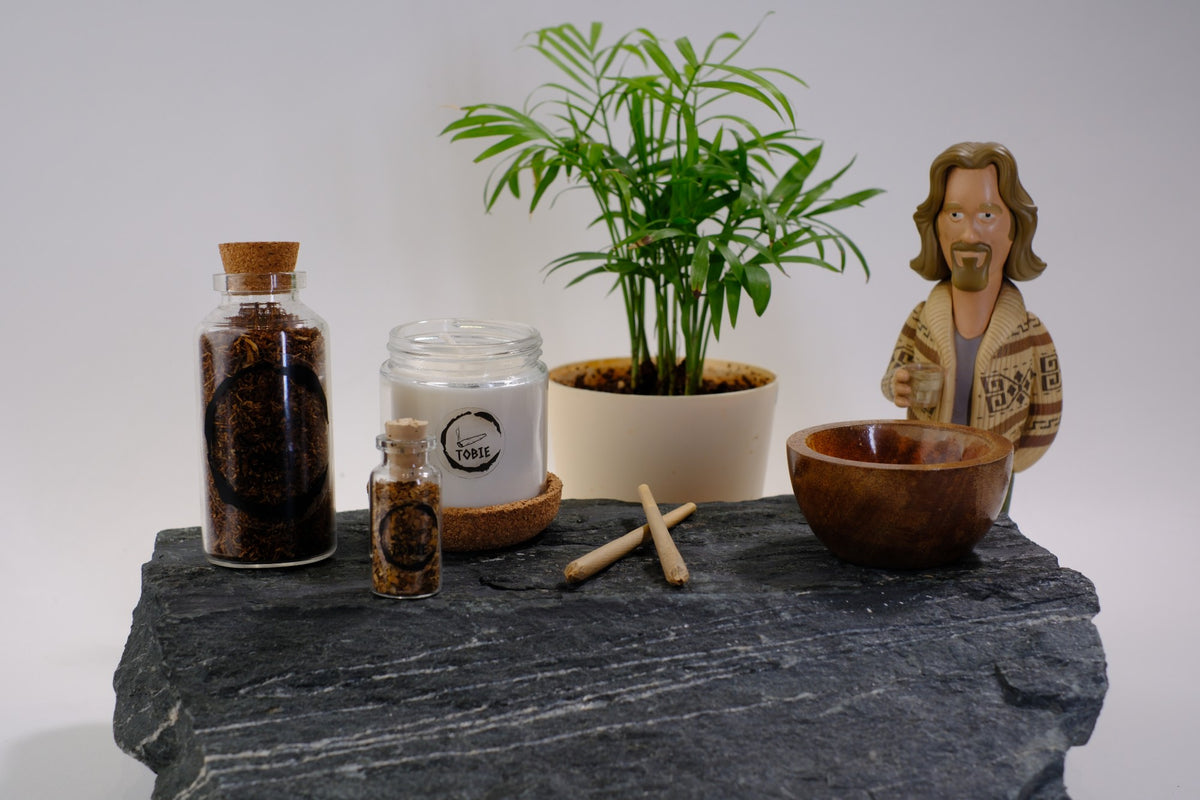 TOBIE ritual still life: cork-sealed blend bottles, aromatic candle, rolled cones and a wooden bowl on slate